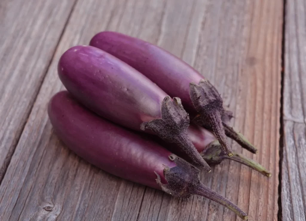 trois aubergines slim jim sont disposées sur une planche en bois elles sont appétissantes