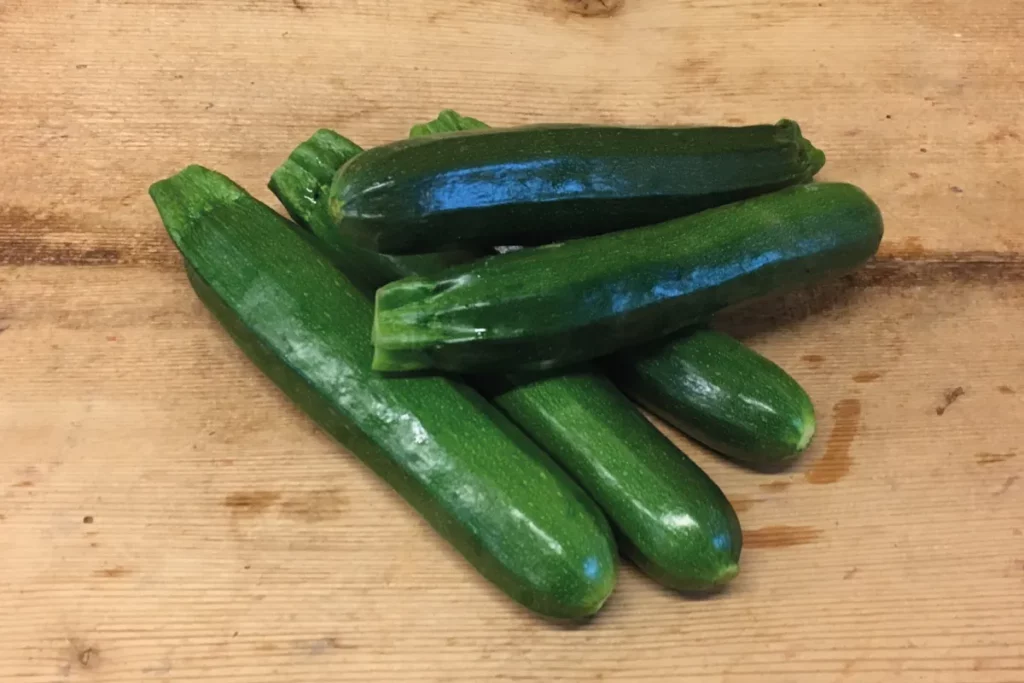 L'image nous montre un tas de courgettes vertes sur une table en bois